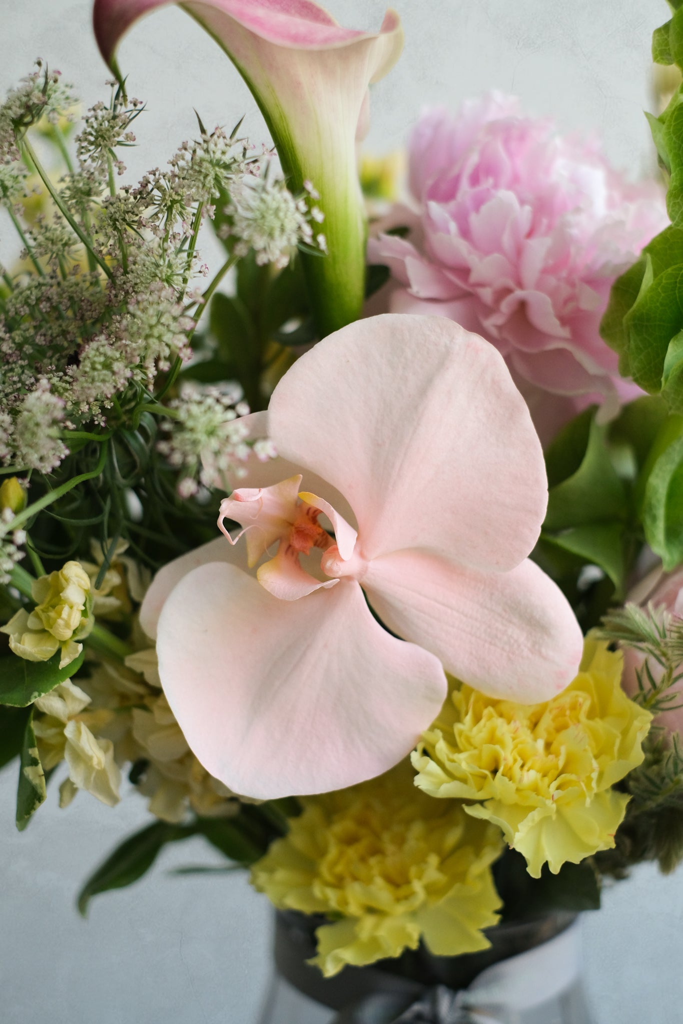 Bouquet of flowers with pink calla lilies and yellow carnations on a light background